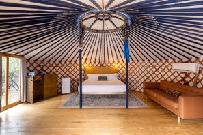 A yurt interior with a bed, a sofa, a chest of drawers, and a small table. - Peaceful Romantic Yurt with Hot Tub in Wimberley, Texas (Wimberley)