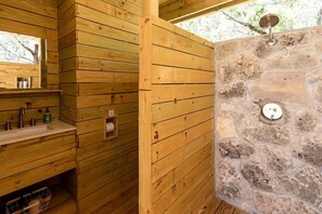 A wooden cabin bathroom with a stone wall, a sink with toiletries, and a mirror.
