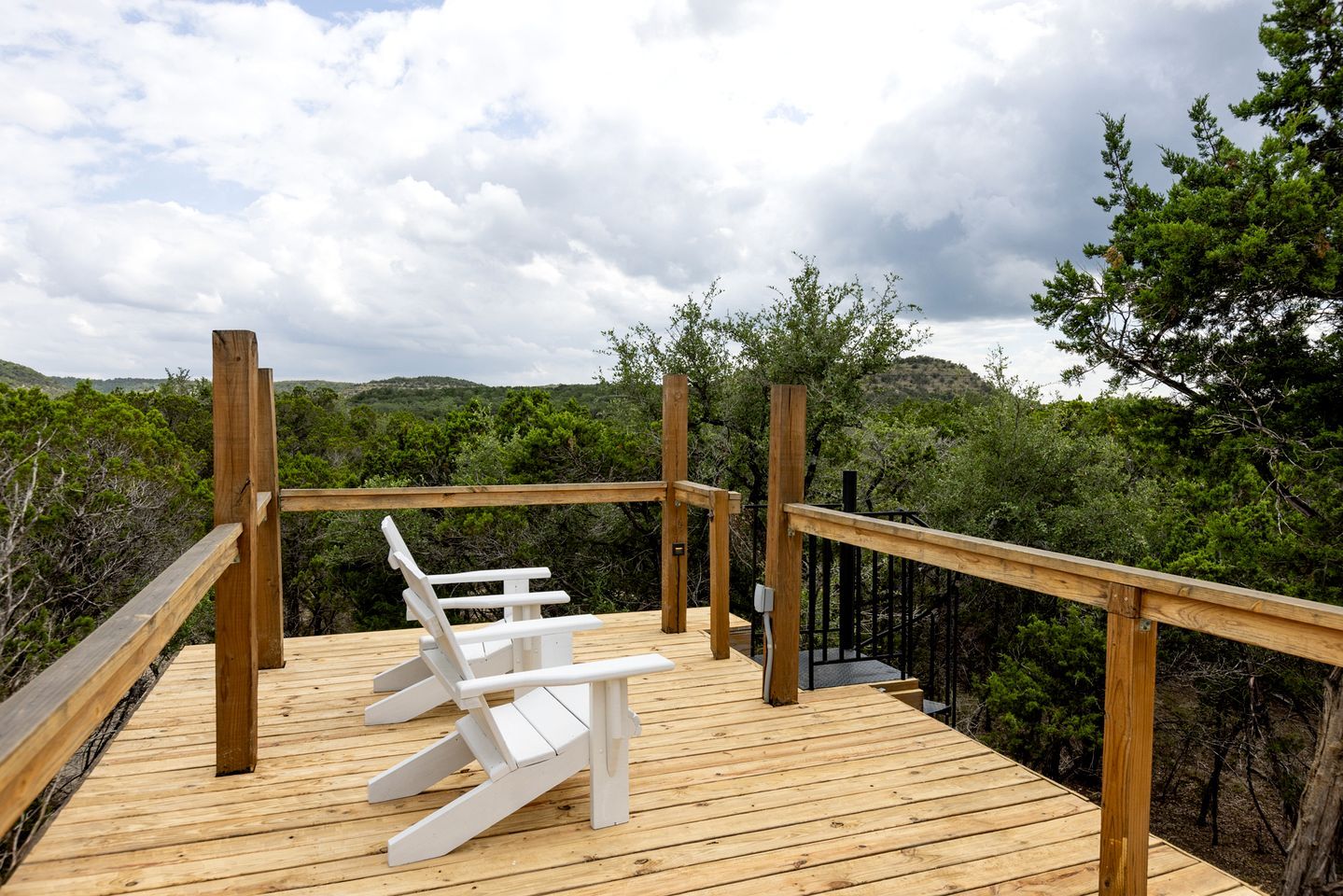 Una terrassa de fusta amb barana, dues cadires Adirondack blanques i vista a una zona boscosa.