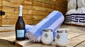 Une terrasse en bois avec un jacuzzi, une bouteille de vin et deux récipients en verre.