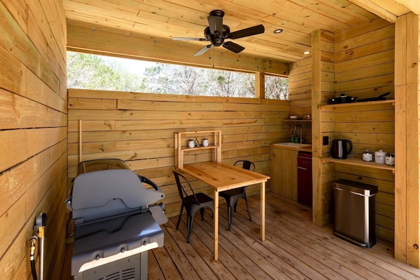 A compact cabin with a wooden interior, a ceiling fan, a table with chairs, a kitchenette, and a small trash bin.
