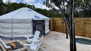 Un espace extérieur abrité avec un foyer, des chaises blanches et une piscine.