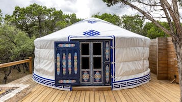 A yurt with a decorative door, a wooden deck, and a natural backdrop.