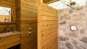 A wooden cabin bathroom with a stone wall, a sink with toiletries, and a mirror. - Peaceful Romantic Yurt with Hot Tub in Wimberley, Texas (Wimberley)