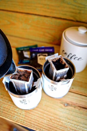 Una cafetera con una taza de café, un termo y una caja de cápsulas de café sobre una superficie de madera.