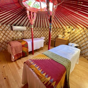 A yurt interior with two beds, a wooden floor, and a central pole structure.