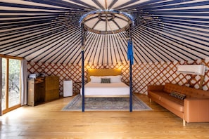 Interior de una yurta con cama, sofá, cómoda y una mesita.