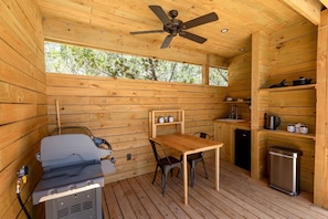 A wooden cabin with a ceiling fan, a grill, a table, chairs, a sink, and a small kitchen area.