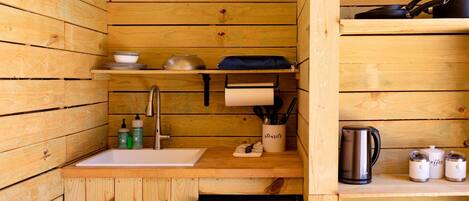 Una cocina de madera compacta con un fregadero, utensilios, una cafetera y un refrigerador Galanz.