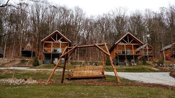 A wooden cabin with a swing set in front, surrounded by trees.