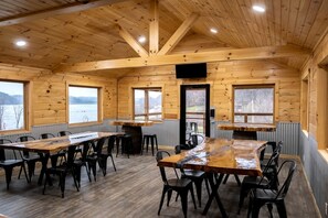 A wooden cabin with a dining area, large windows, and a view of a lake.