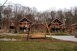 A wooden cabin with a swing set in front, surrounded by trees.