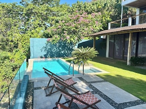 Une piscine avec deux chaises longues, entourée d’une pelouse bien entretenue et de différentes espèces d’arbres.