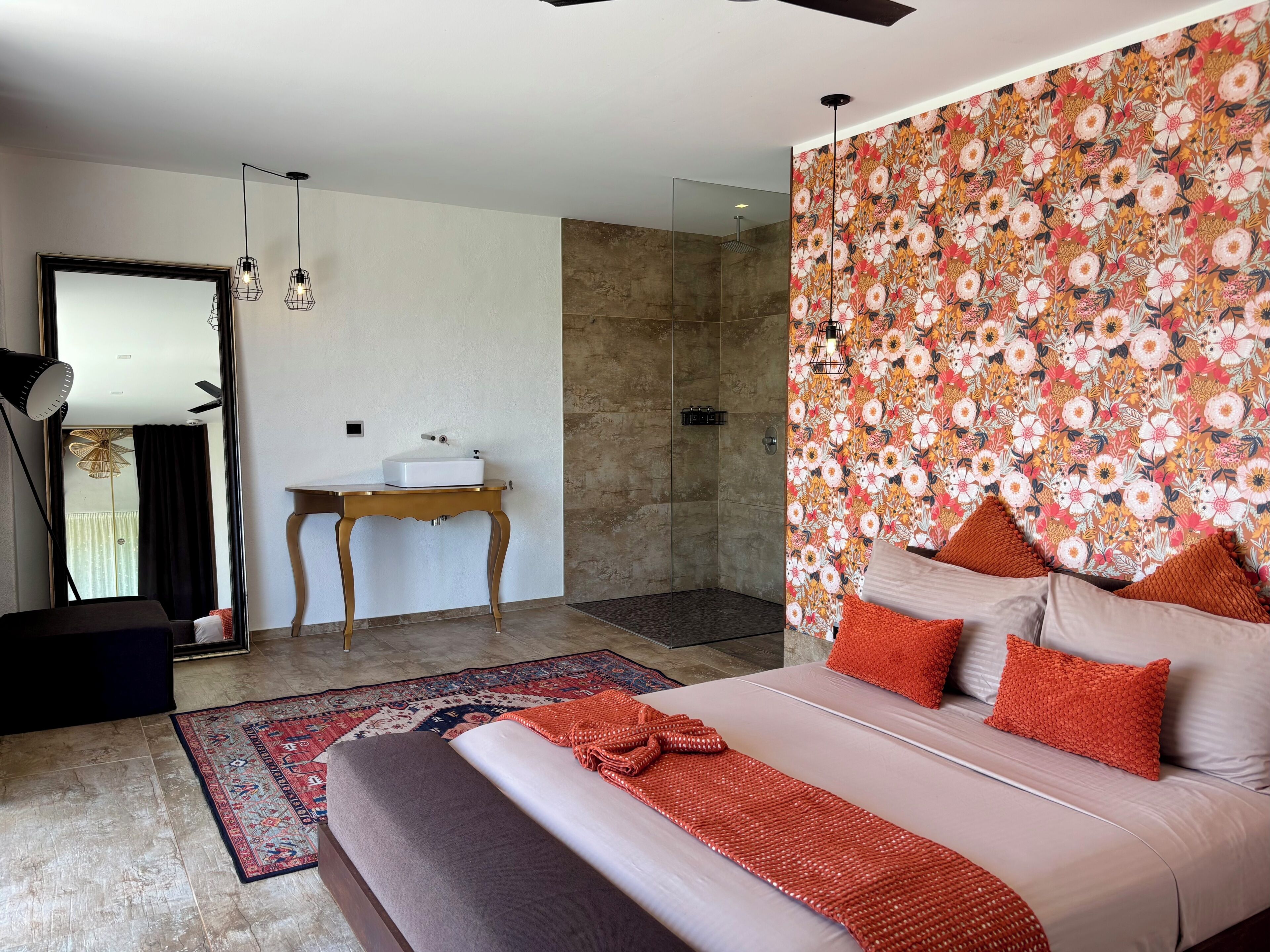 A modern bedroom with a large bed, a small bedside table, a mirror, and a shower area.