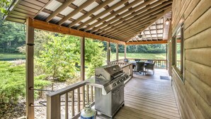 Eine überdachte Terrasse im Freien mit Grill, Sitzgelegenheit und Blick auf eine natürliche Landschaft.