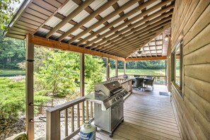 A covered outdoor deck with a grill, seating area, and a view of a natural landscape.