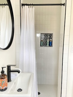 A bathroom with a shower curtain, a sink with a soap dispenser, and a tiled shower area.