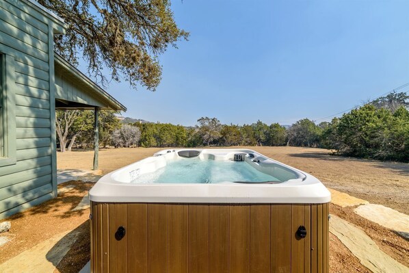 Ein Whirlpool in einem Hinterhof mit einer Holzterrasse, einem Haus und Bäumen im Hintergrund.