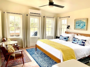 A bedroom with a bed, a table with chairs, a ceiling fan, and a window with curtains.