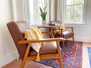 Ein Zimmer mit braunem Ledersessel, einem kleinen runden Tisch, einer Topfpflanze und einem gemusterten Teppich.