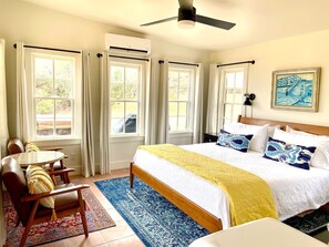 A bedroom with a bed, a table with chairs, a ceiling fan, and a window with curtains.