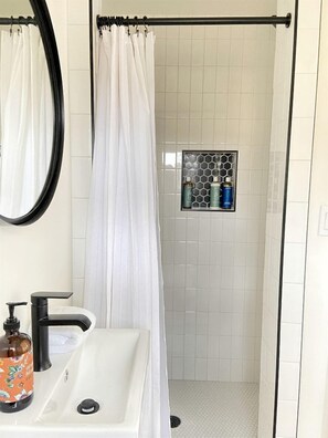 A bathroom with a shower curtain, a sink with a soap dispenser, and a tiled shower area.