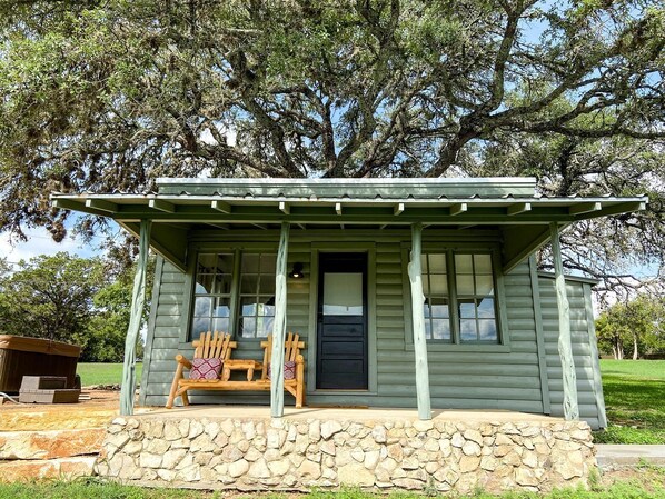 A small, single-story cabin with a porch, a bench, and a stone foundation.