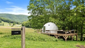 A geodesic dome structure with a wooden deck, surrounded by lush greenery and hills. - Outstanding Chic Dome with Private Deck in North Carolina (Creston)