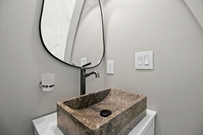 Un baño con un lavamanos de piedra rectangular, un grifo moderno, un espejo montado en la pared y un inodoro blanco.