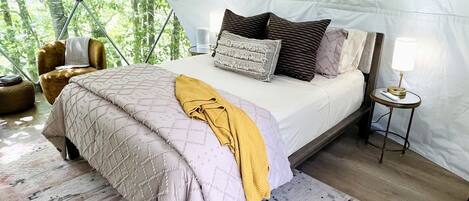 Alojamiento en tienda de campaña con cama, almohadas, lámpara, silla y alfombra.