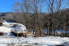 Un espace extérieur enneigé doté d’une structure en forme de dôme, d’une terrasse en bois et d’un chemin menant à cet espace.