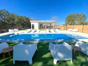 Piscina con sillas de descanso y una zona de estar cubierta.