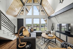 A spacious loft with a high ceiling, large windows, a staircase, and modern furnishings. - Family-Friendly A-frame with Outdoor Camp Fire in Texas (New Braunfels)