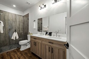 Un baño moderno con ducha, inodoro y tocador con un espejo grande.