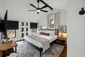 A bedroom with a bed, a desk, a TV, a ceiling fan, and boots on the wall. - Family-Friendly A-frame with Outdoor Camp Fire in Texas (New Braunfels)