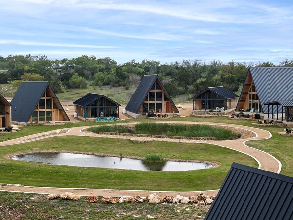 A series of modern cabins with sloped roofs, surrounded by a landscaped area with a pond and walking paths.