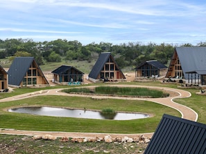 A series of modern cabins with sloped roofs, surrounded by a landscaped area with a pond and walking paths.