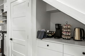 A kitchen with a coffee maker, a kettle, and a coffee pod holder.