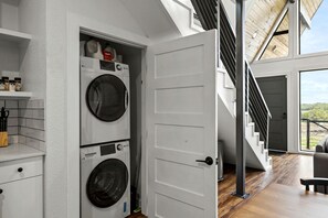 A laundry room with two stacked washing machines, a white door, and a staircase leading to an upper level. - Family-Friendly A-frame with Outdoor Camp Fire in Texas (New Braunfels)
