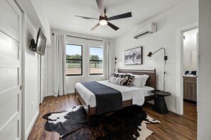 A bedroom with a bed, a ceiling fan, a window, a mounted TV, and a cowhide rug. - Family-Friendly A-frame with Outdoor Camp Fire in Texas (New Braunfels)