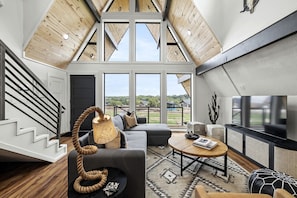 A spacious loft with a high ceiling, large windows, a staircase, and modern furnishings.