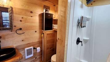 A wooden cabin bathroom with a toilet, sink, and shower.