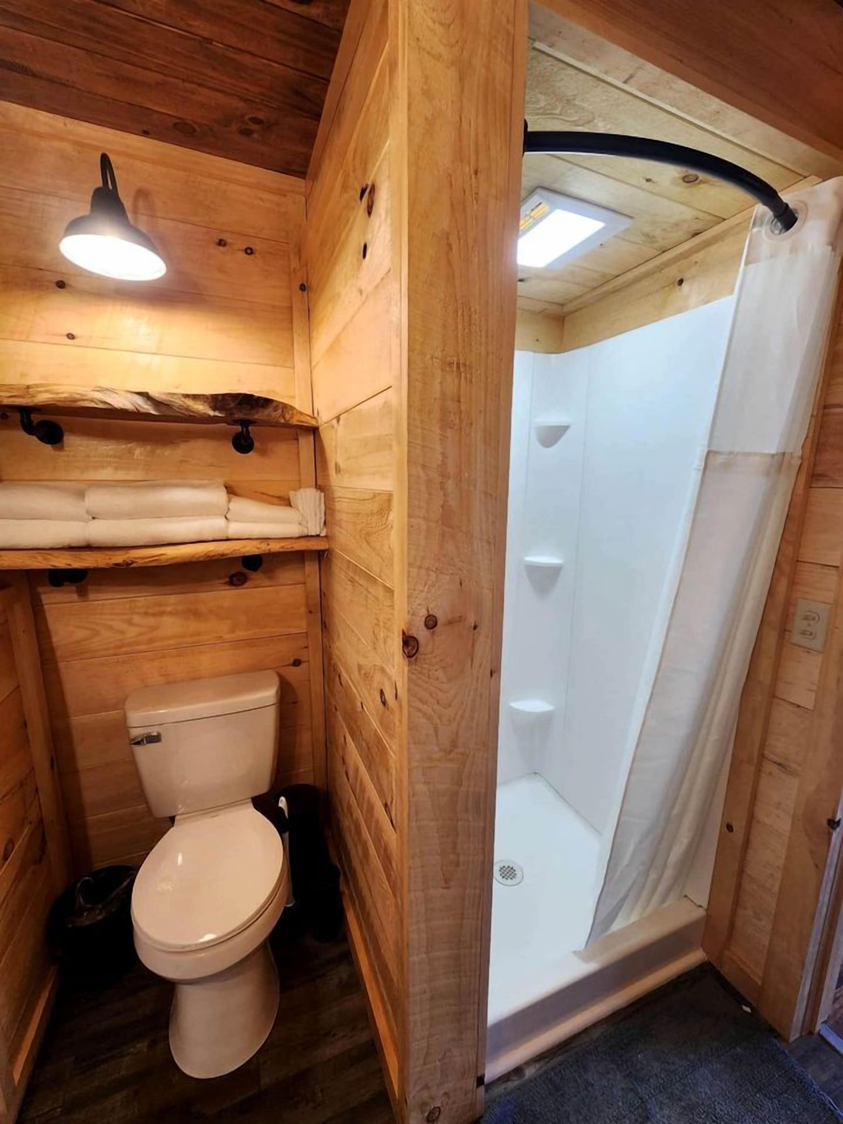 A wooden interior with a toilet, a shower, and a hanging light fixture.