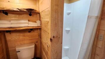 A wooden interior with a toilet, a shower, and a hanging light fixture.