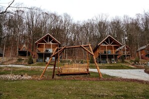 Une cabane en bois avec une balançoire devant, entourée d’arbres.