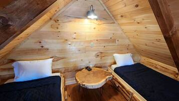 Ein gemütliches Schlafzimmer im Dachgeschoss mit Holzwänden und schräger Decke, ausgestattet mit zwei Betten, einem kleinen runden Tisch und einer einzelnen Lampe.