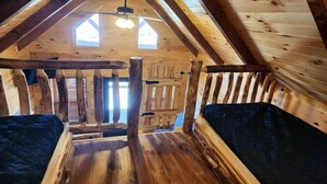 Ein Schlafzimmer im Blockhaus-Stil mit Dachschräge, zwei Fenstern und einem zentralen Holzbalken.