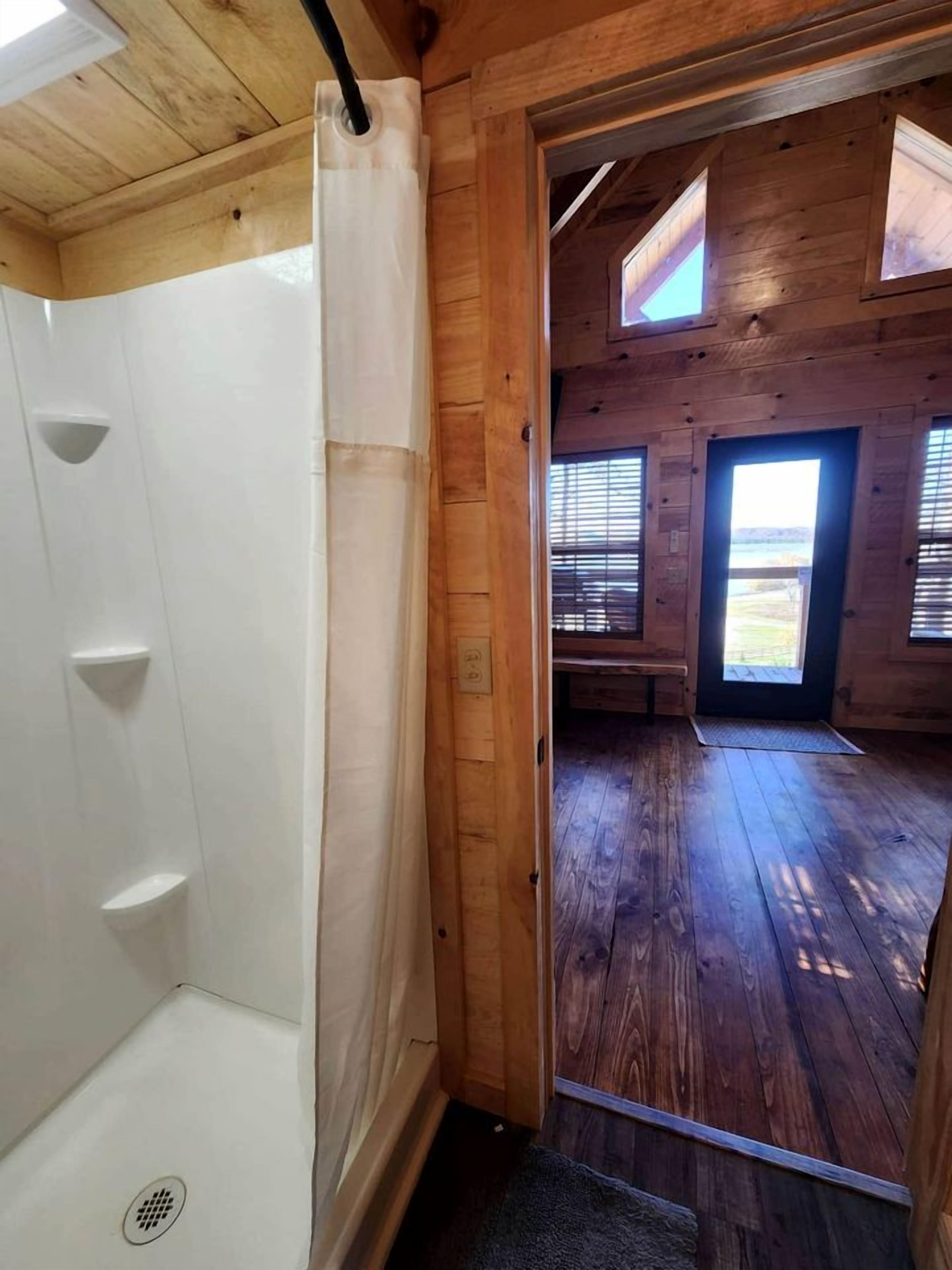 A wooden interior with a shower, a door leading to a room with a view, and a window with blinds.
