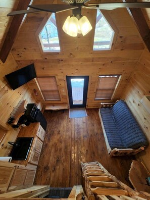 A cabin with a loft bedroom, a kitchenette, and a large window.