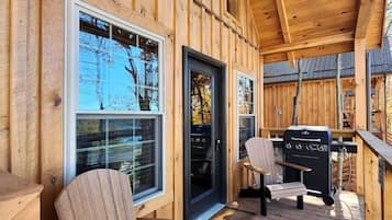 A wooden deck with a grill and chairs, a door, and windows.